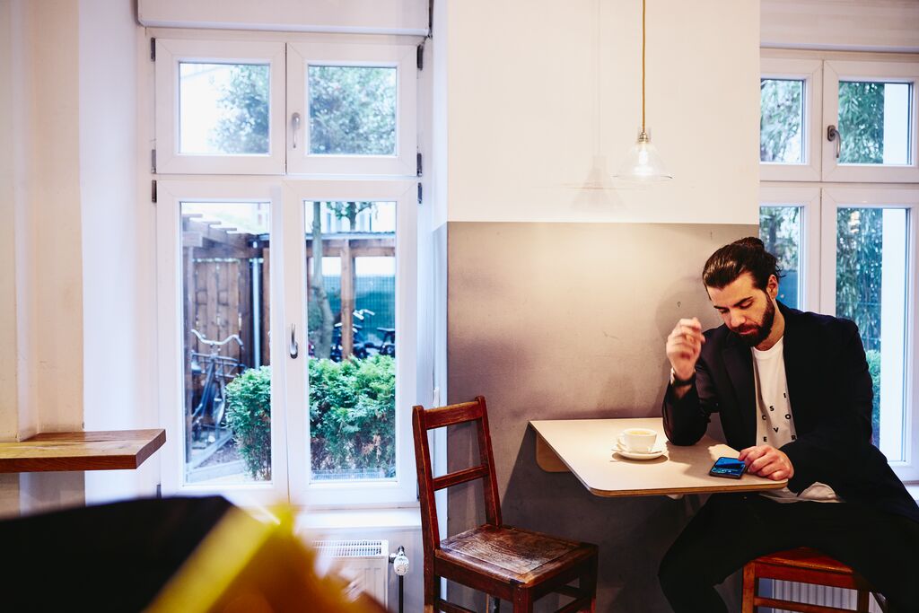 en man sitter vid bordet med en kaffe, ser allvarligt ner på sin mobiltelefon